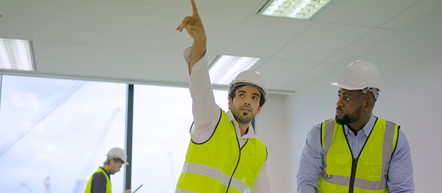 Contractors discussing and gesturing at the ceiling lighting in a commercial office building